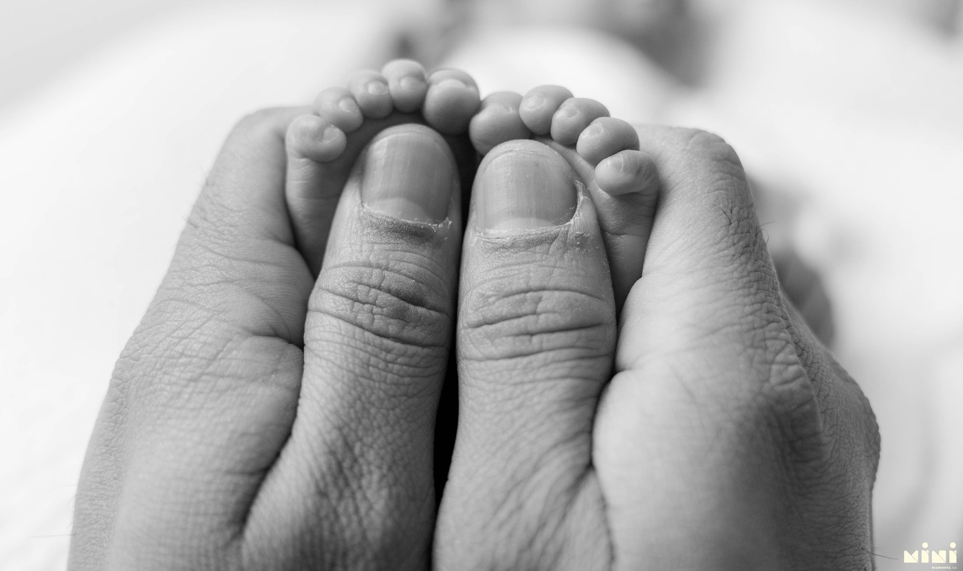 Newborn tiny feet in parent hands — black and white newborn photography UK Mini Momentz