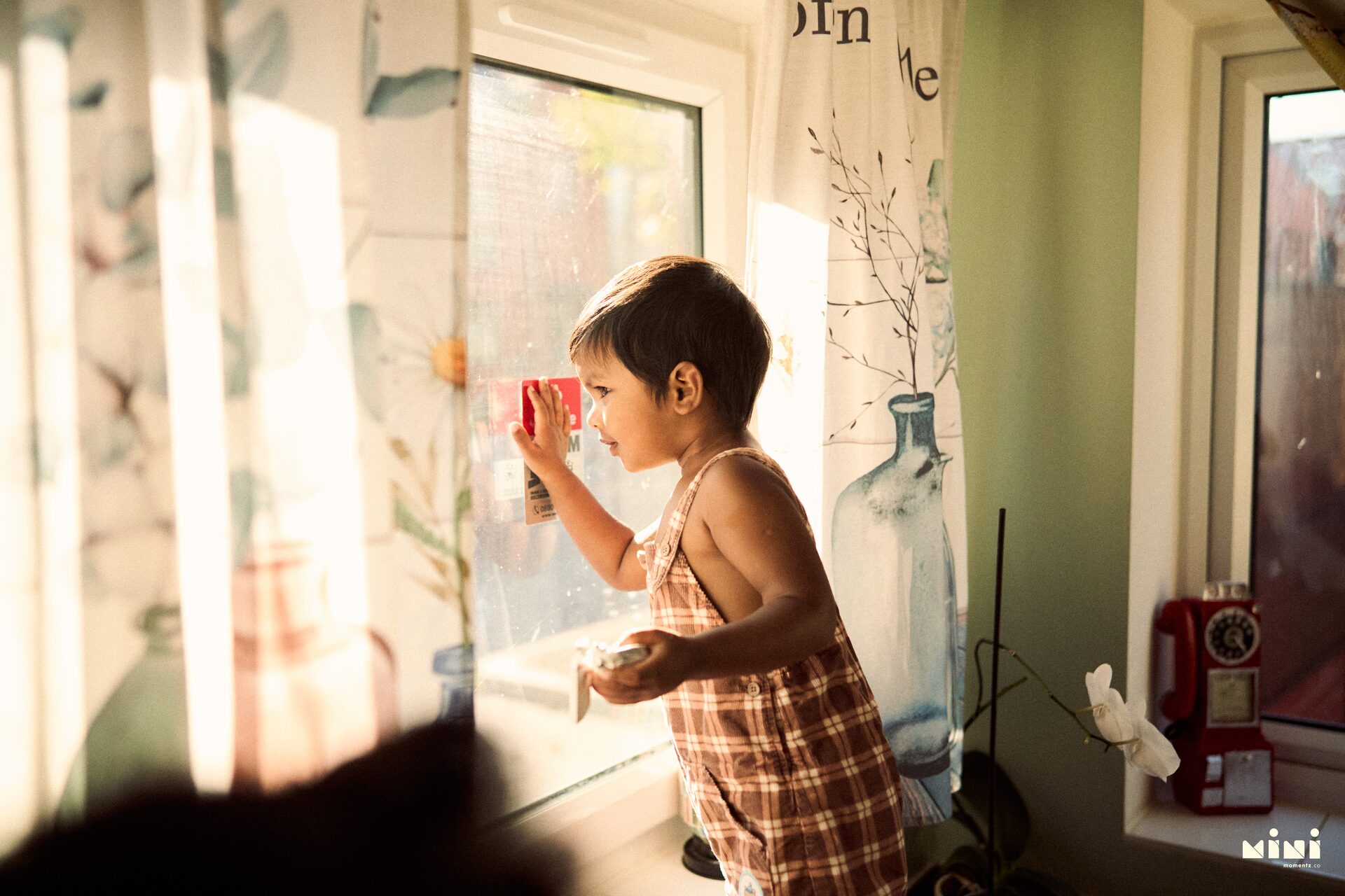 Aaru standing at the window in golden afternoon light at home in Leicester — quiet toddler portrait by Mini Momentz