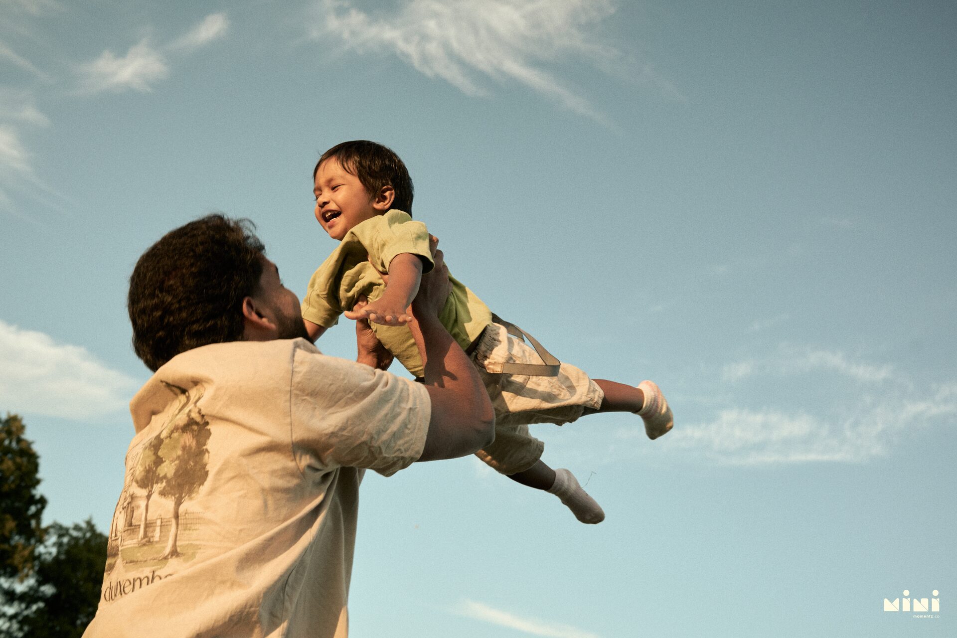 Father throwing toddler son joyfully into the air at Victoria Park Leicester