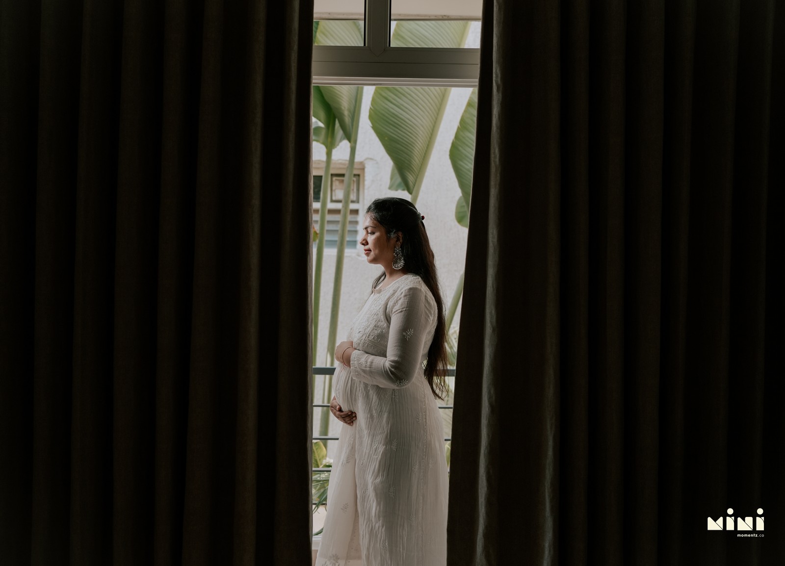 Deepti maternity photography — standing by window in natural light. South Indian maternity photographer UK Mini Momentz