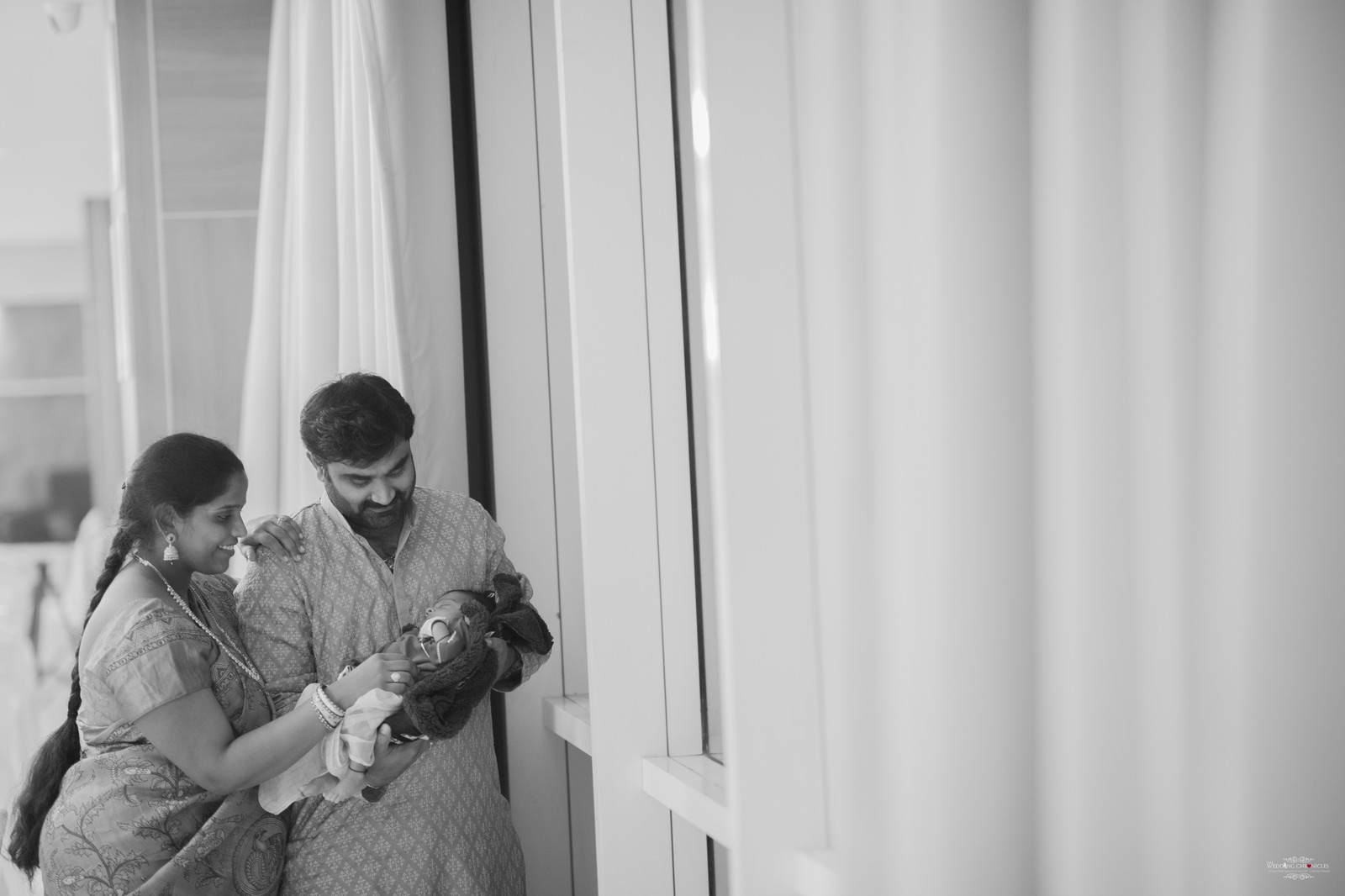 New parents with newborn beside a window in black and white