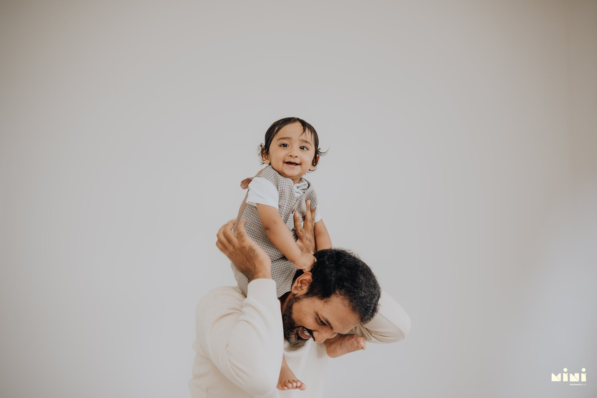 Sid sitting on Ramesh's shoulders, laughing — playful father and son portrait by Mini Momentz family photographer Leicester